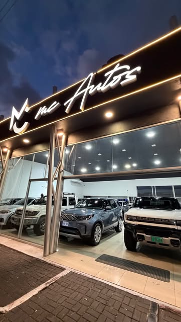 Fachada iluminada del showroom MC Autos de noche, con vehículos en exhibición